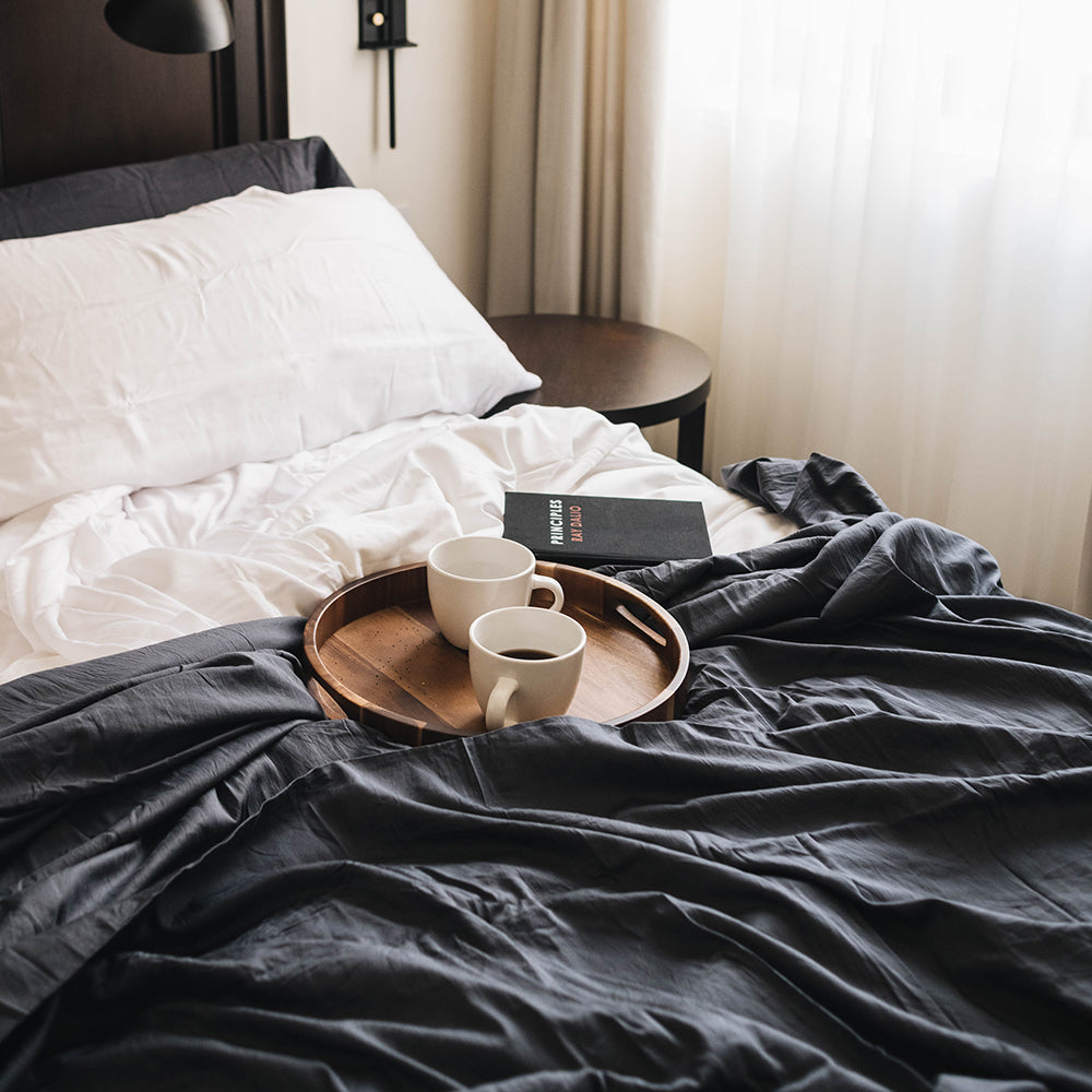 Closeup of eucalyptus sheets in dark slate gray and white, with breakfast tray of coffees on top