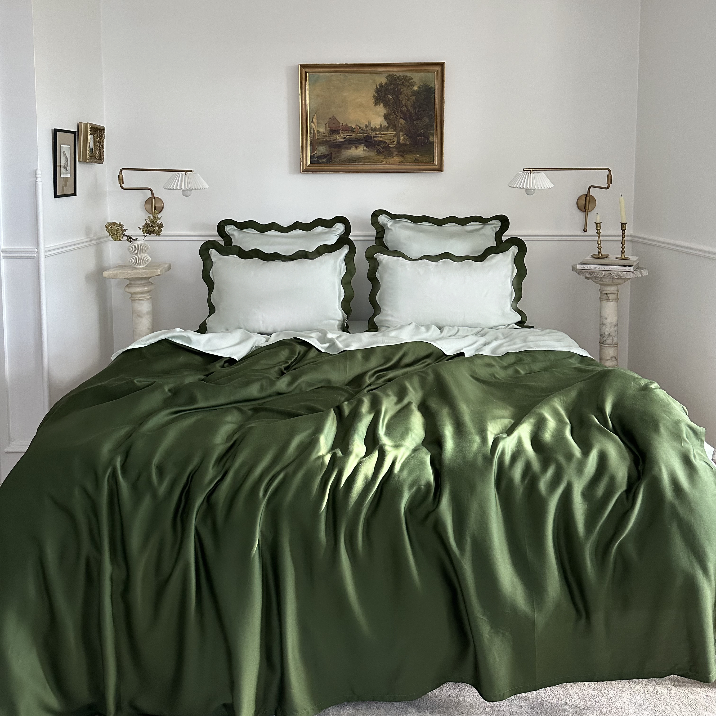 Bedroom with eucalyptus tencel bedding in with dark green and light green scalloped pillows, framed artwork on the wall.