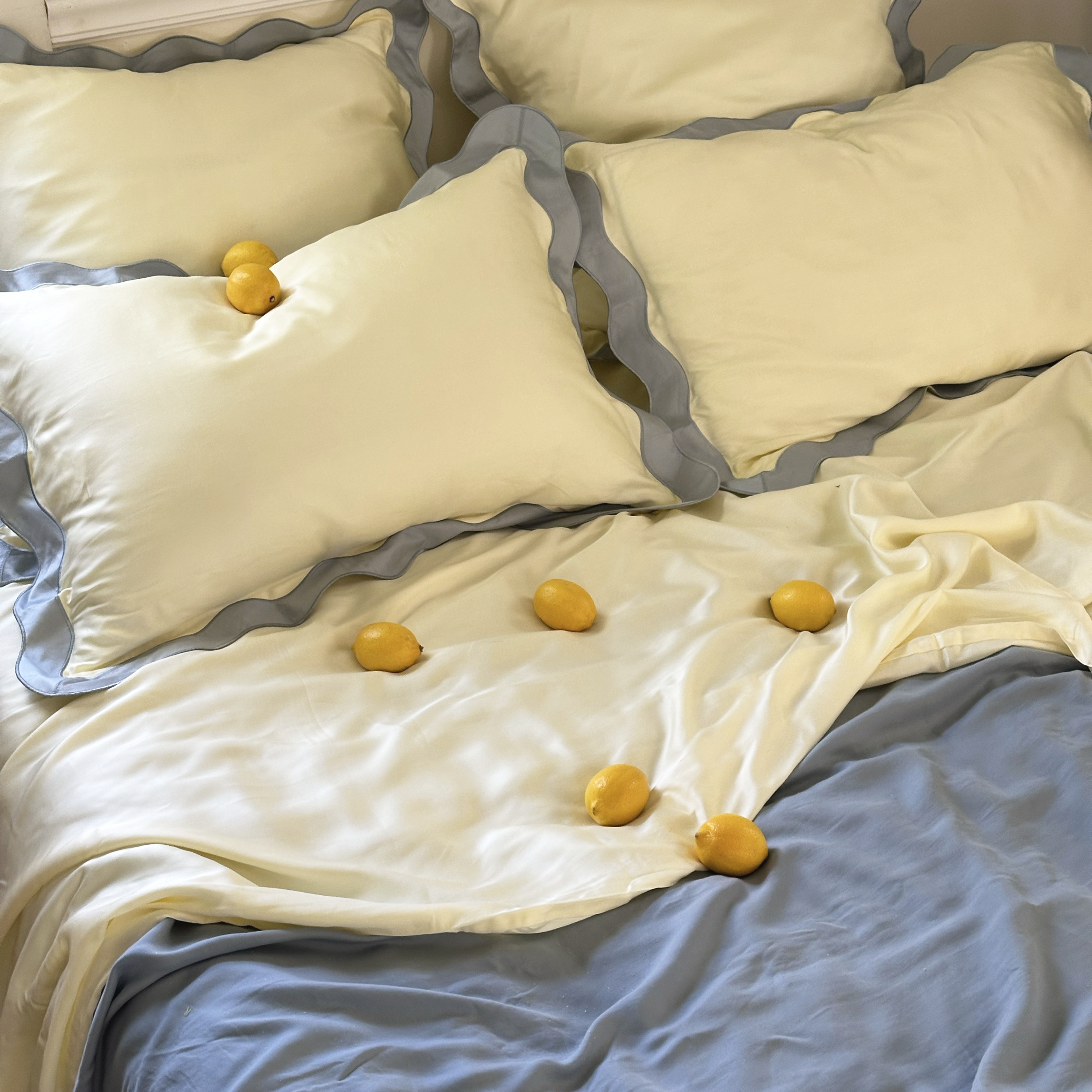 Butter yellow and light blue scalloped eucalyptus tencel pillows on a bed with light blue eucalyptus sheets with lemons.