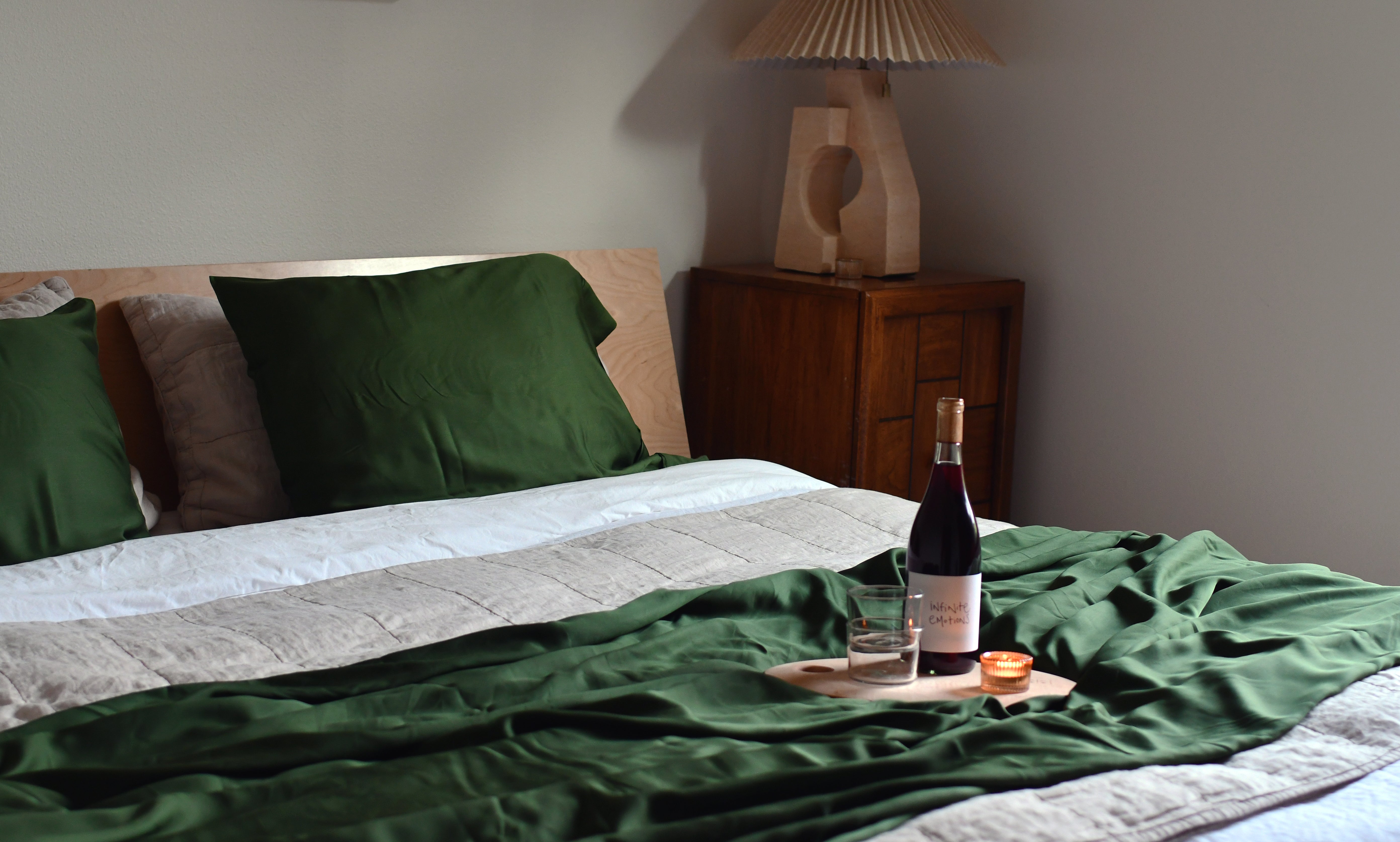 Closeup of dark emerald green eucalyptus sheets styled in bed with bottle of white and lit candle