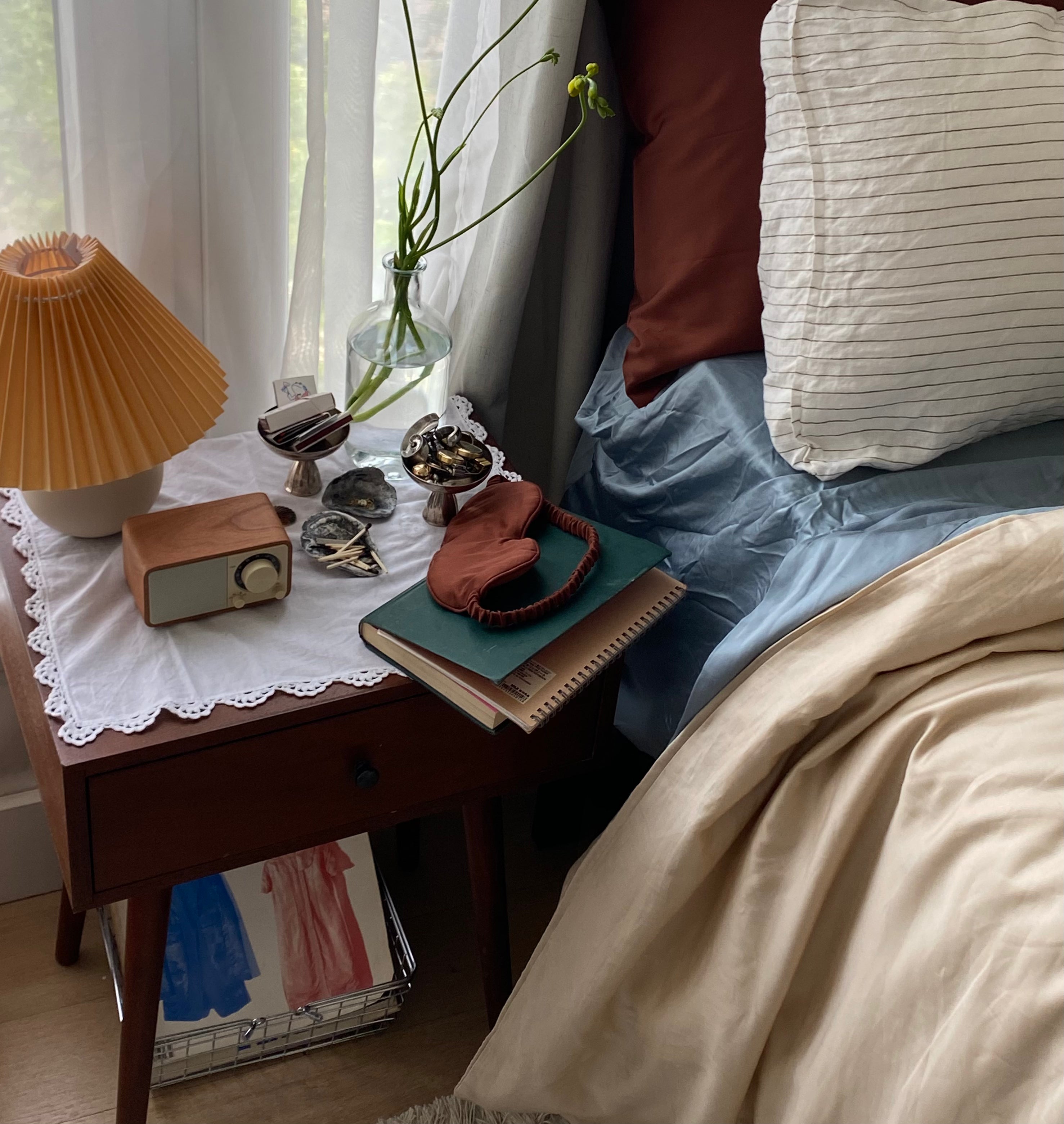 Close up of night stand with eucalyptus terracotta sleep mask and bed styled with terracotta and blue cooling eucalyptus tencel sheets