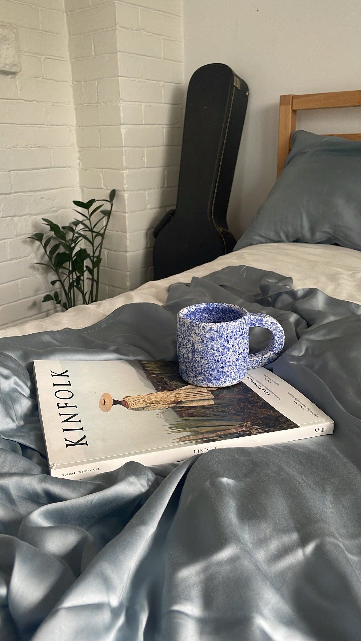 eucalyptus sheets close up styled in bed to show the silky texture in light blue and white with magazine and mug