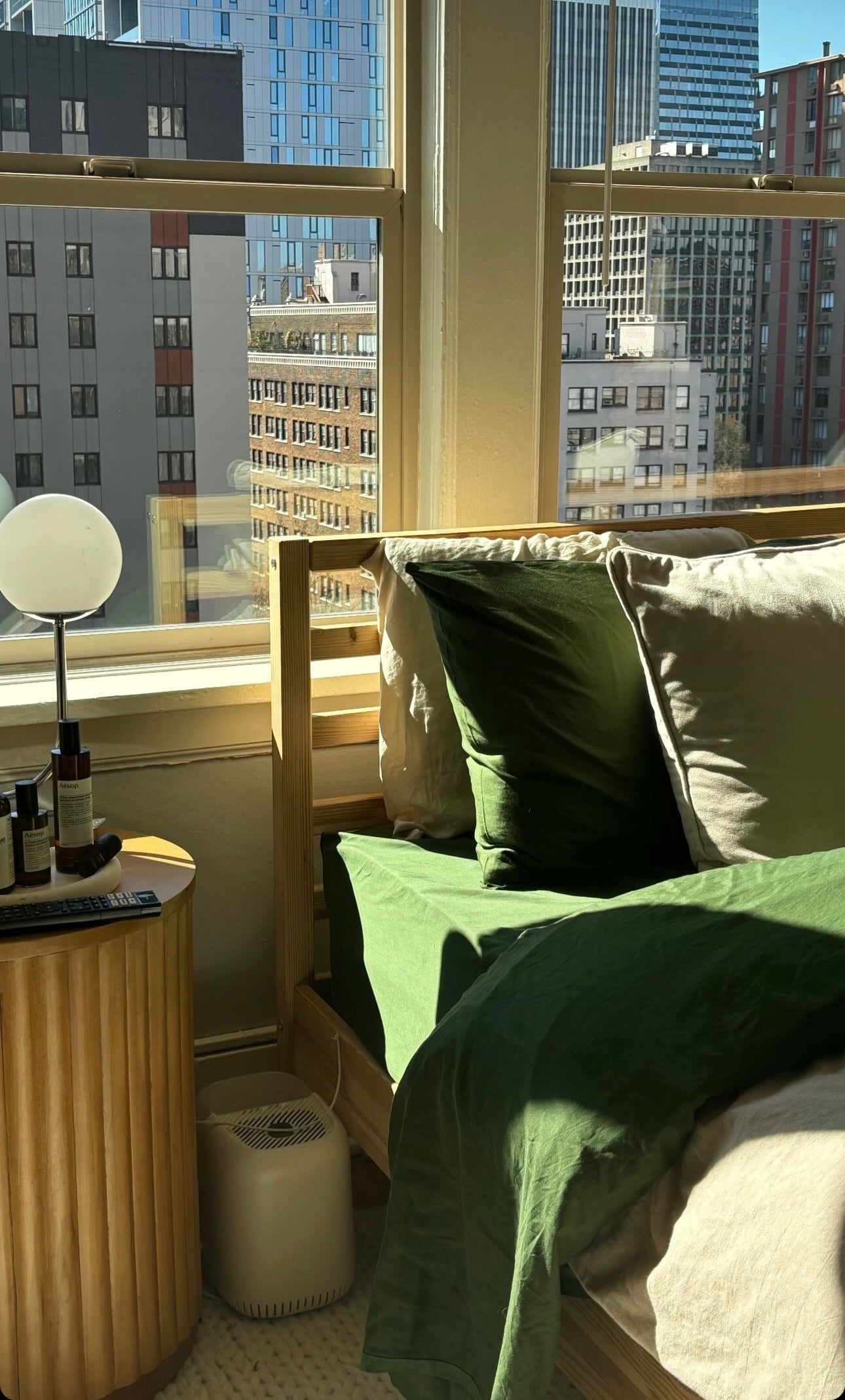 High rise bedroom with city view and emerald green and beige eucalyptus sheets in bed
