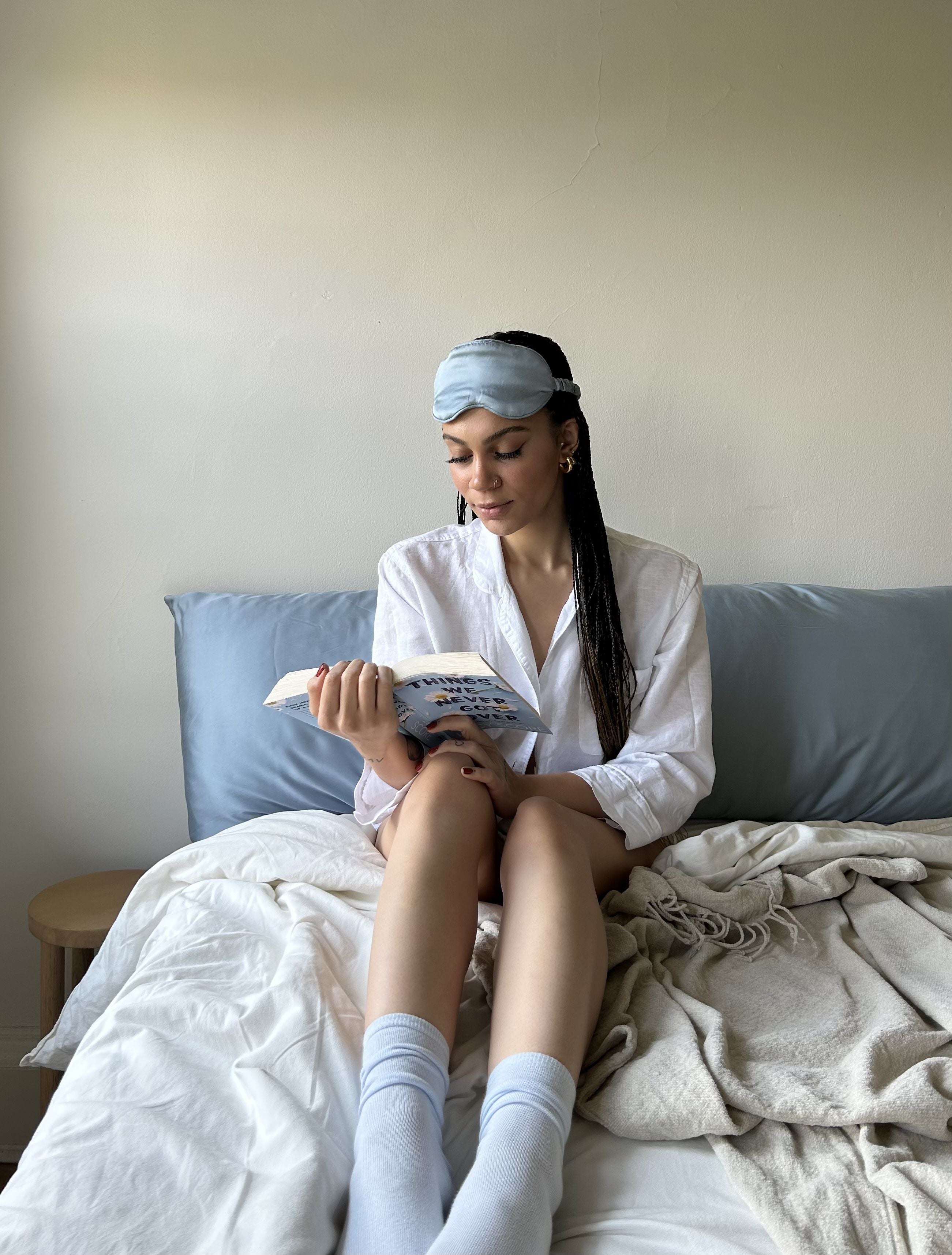 Girl reading in bed with eucalyptus blue sleep mask and cooling eucalyptus tencel sheets that's blue and beige