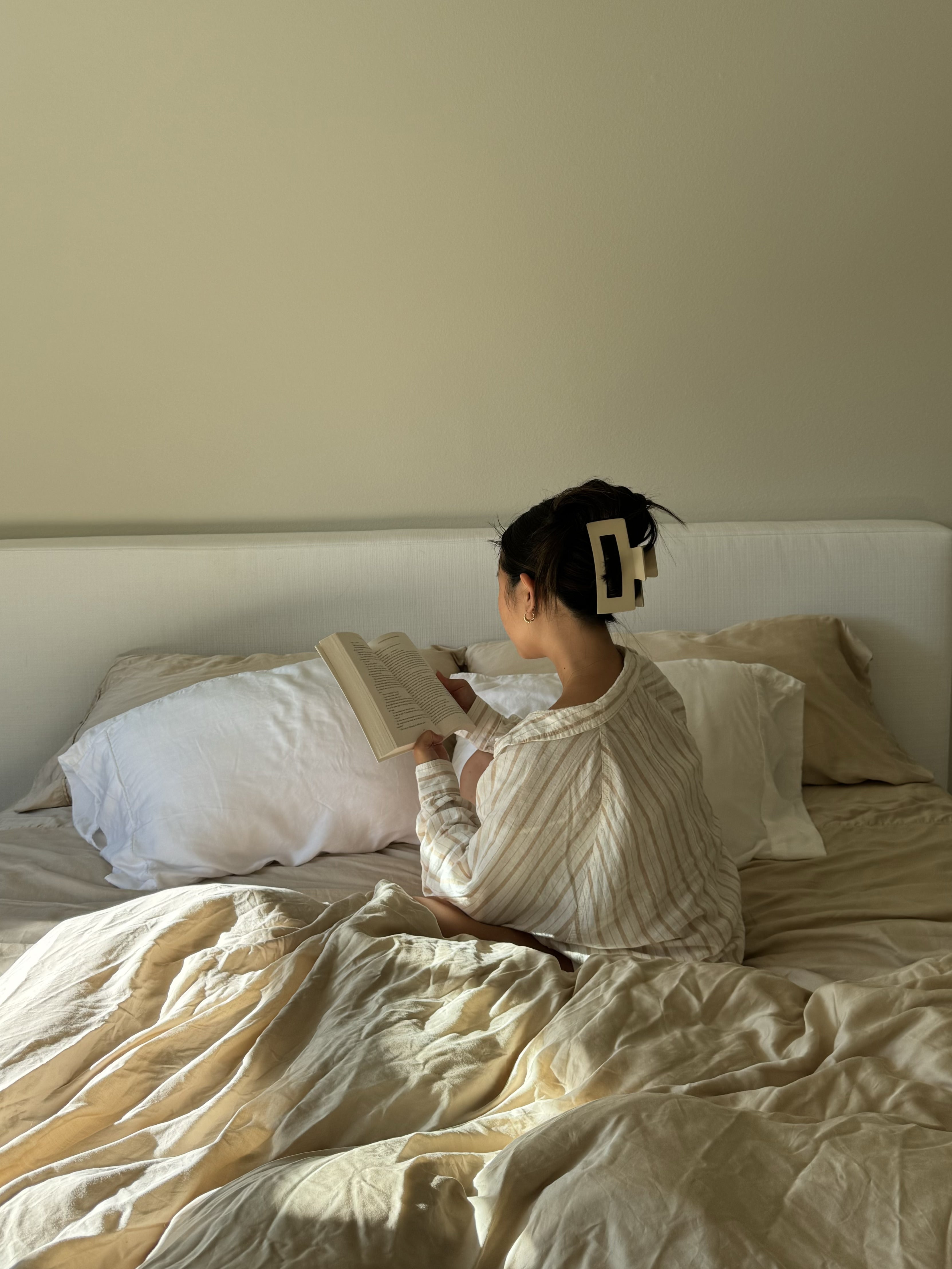 Woman reading in bed styled with neutral eucalyptus lyocell sheets and breathable bedding for better sleep