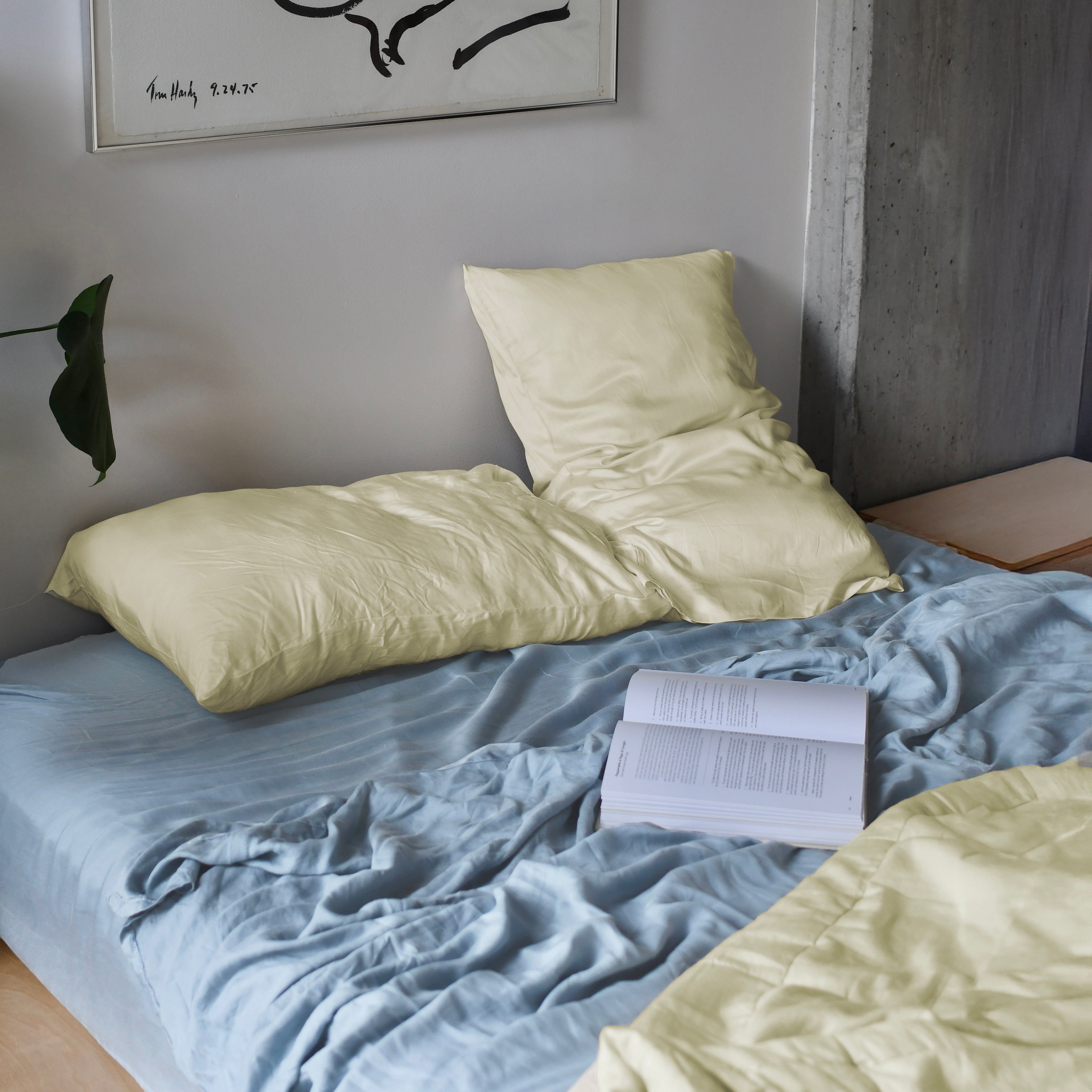 silky soft eucalyptus tencel sheets in yellow and blue styled in bed with a book showcasing its silky texture