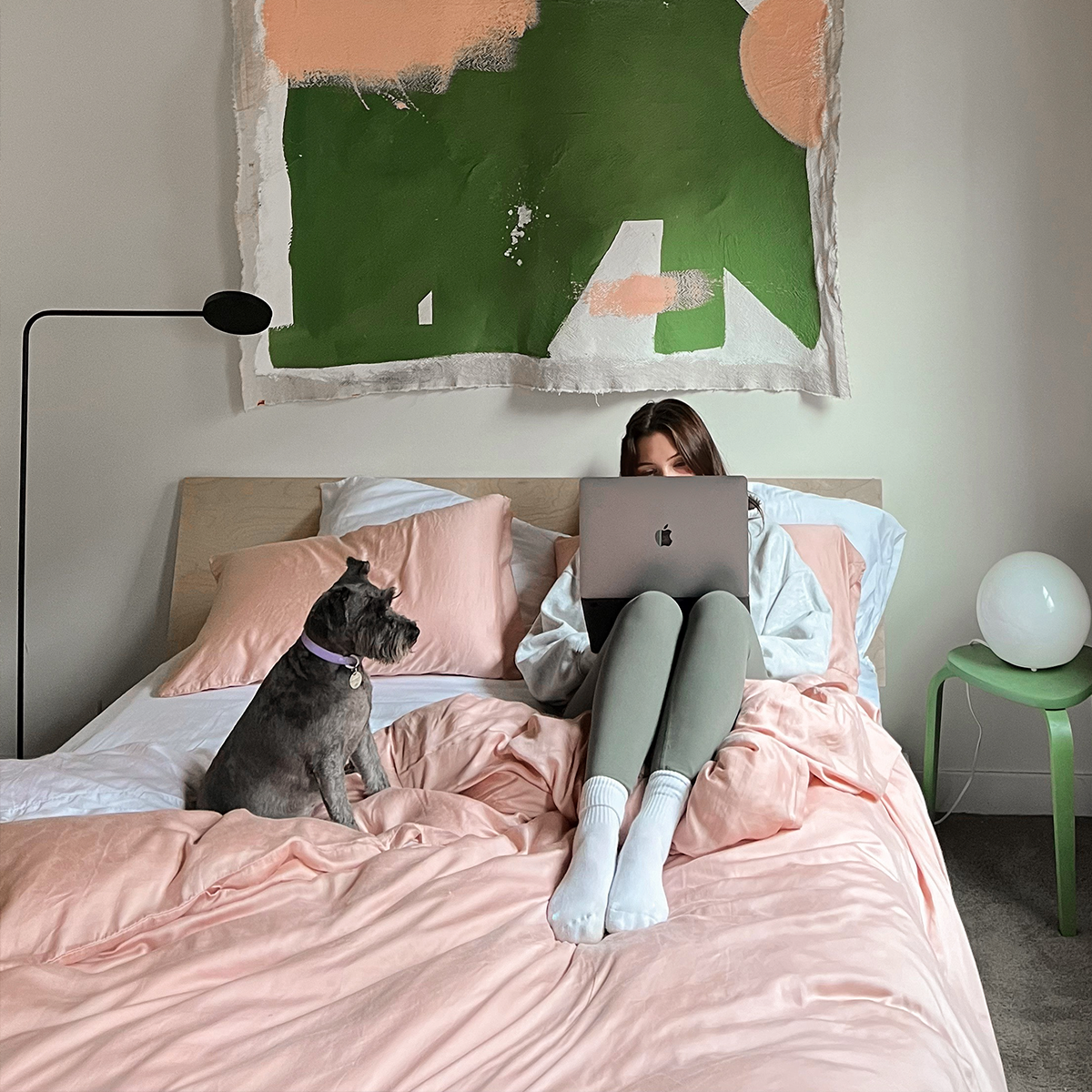 Girl in bed doing work on her laptop with her dog next to her, in cozy eucalyptus sheets in pink and white