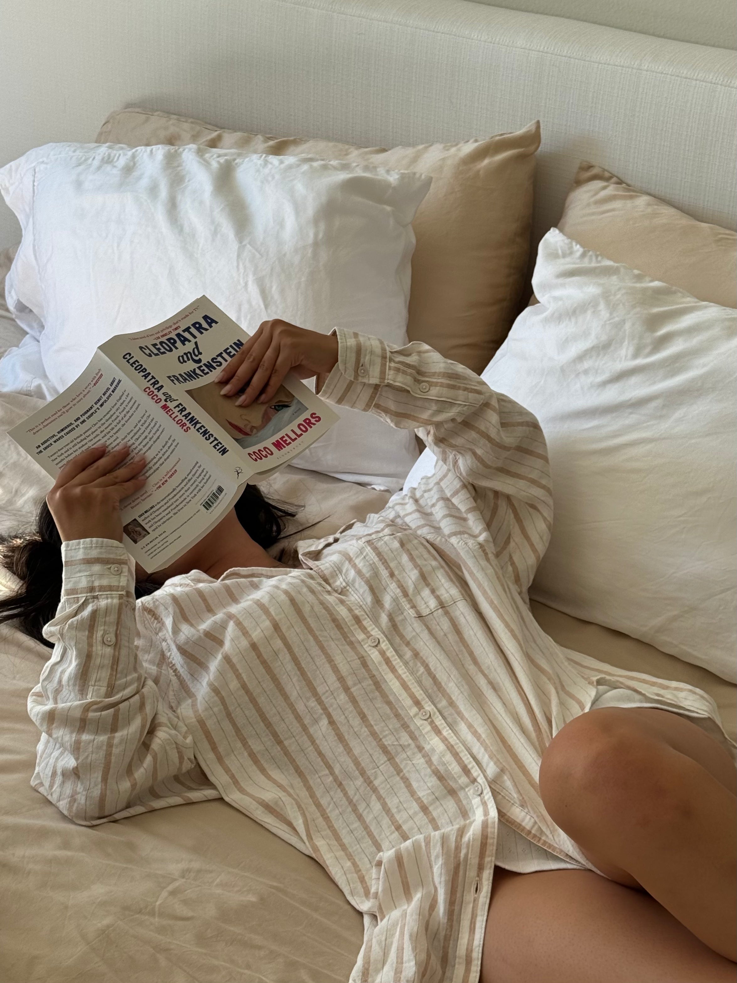 girl reading a book laying in ultra soft white and beige sheets in bed