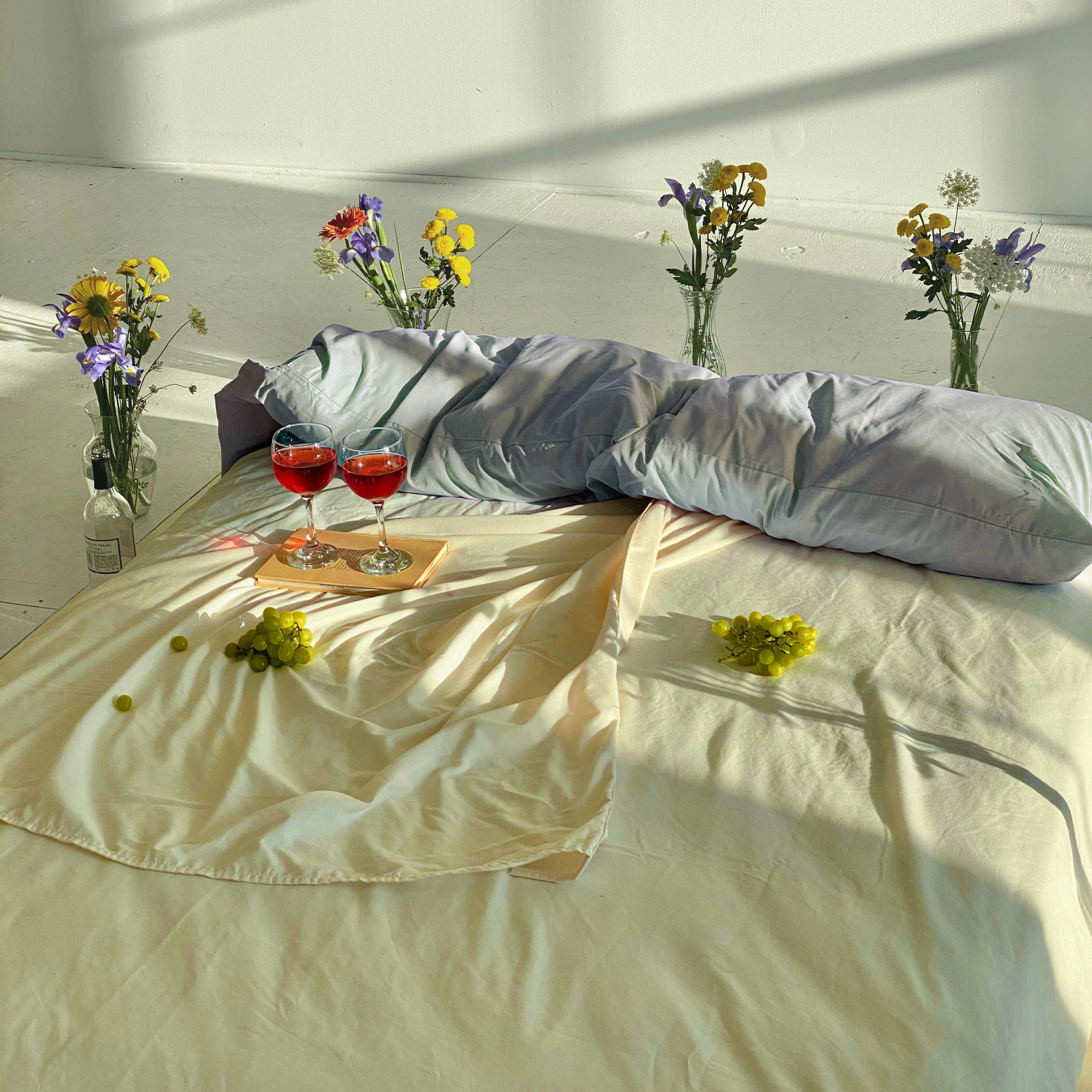 A bed styled with cooling yellow and light blue eucalyptus tencel sheets with flowers surrounding the bed