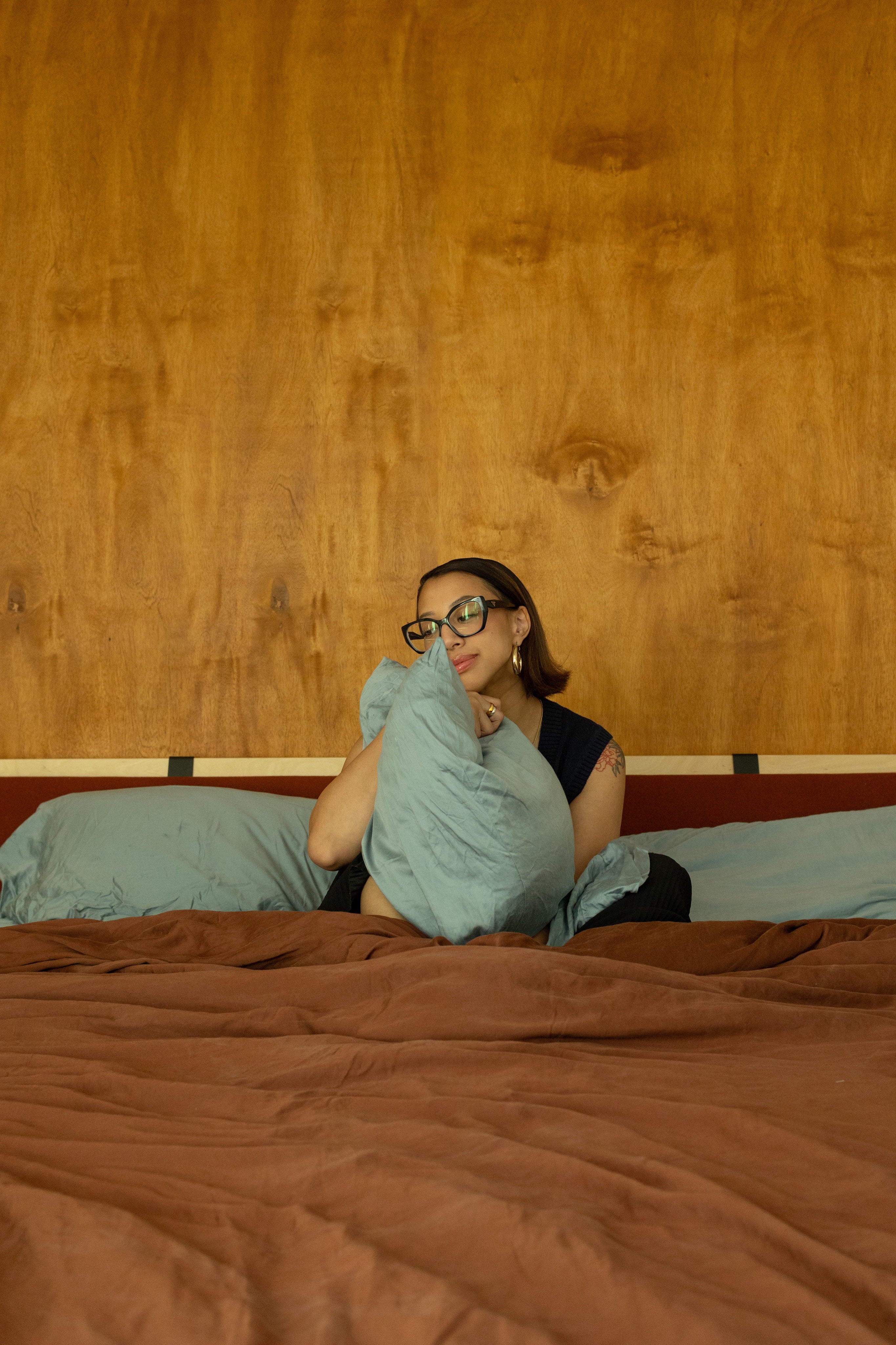 eucalyptus tencel sheets and terracotta and blue styled in bed with girl sitting in bed holding blue pillow